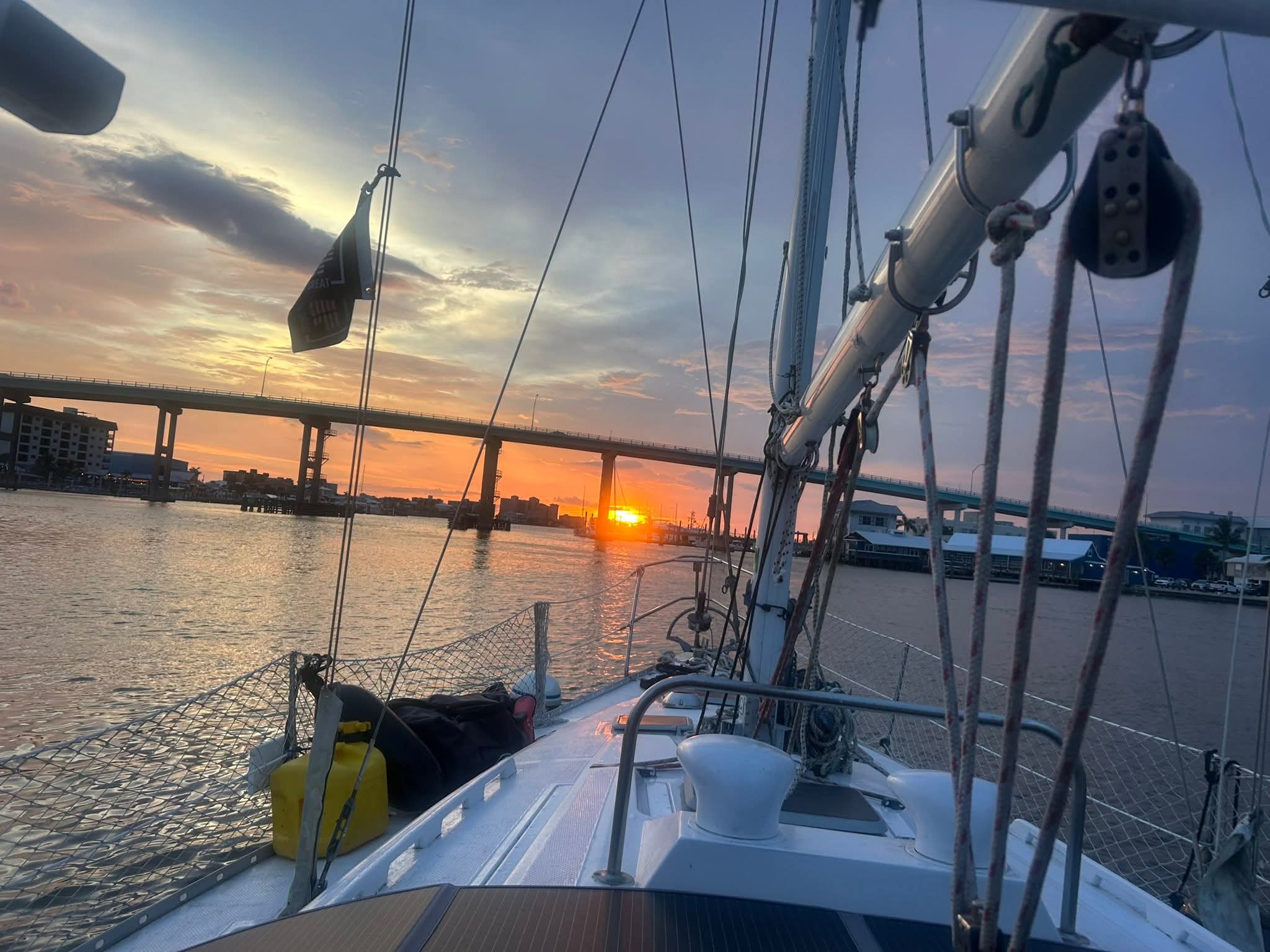 Sailboat deck view of a vibrant sunset behind a bridge over calm coastal waters.