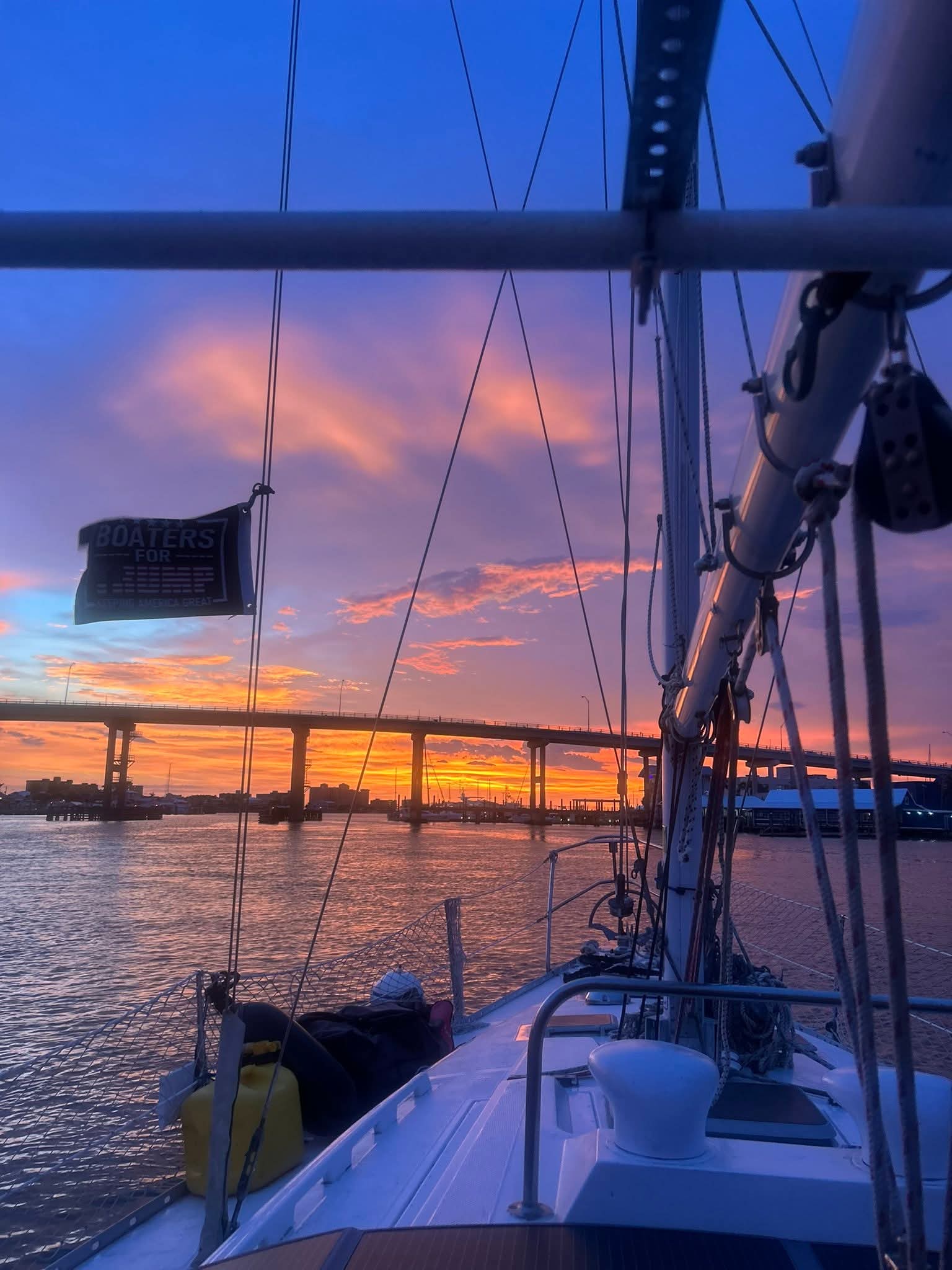 Sailboat deck view of a bridge silhouetted against a vibrant orange and purple sunset sky.