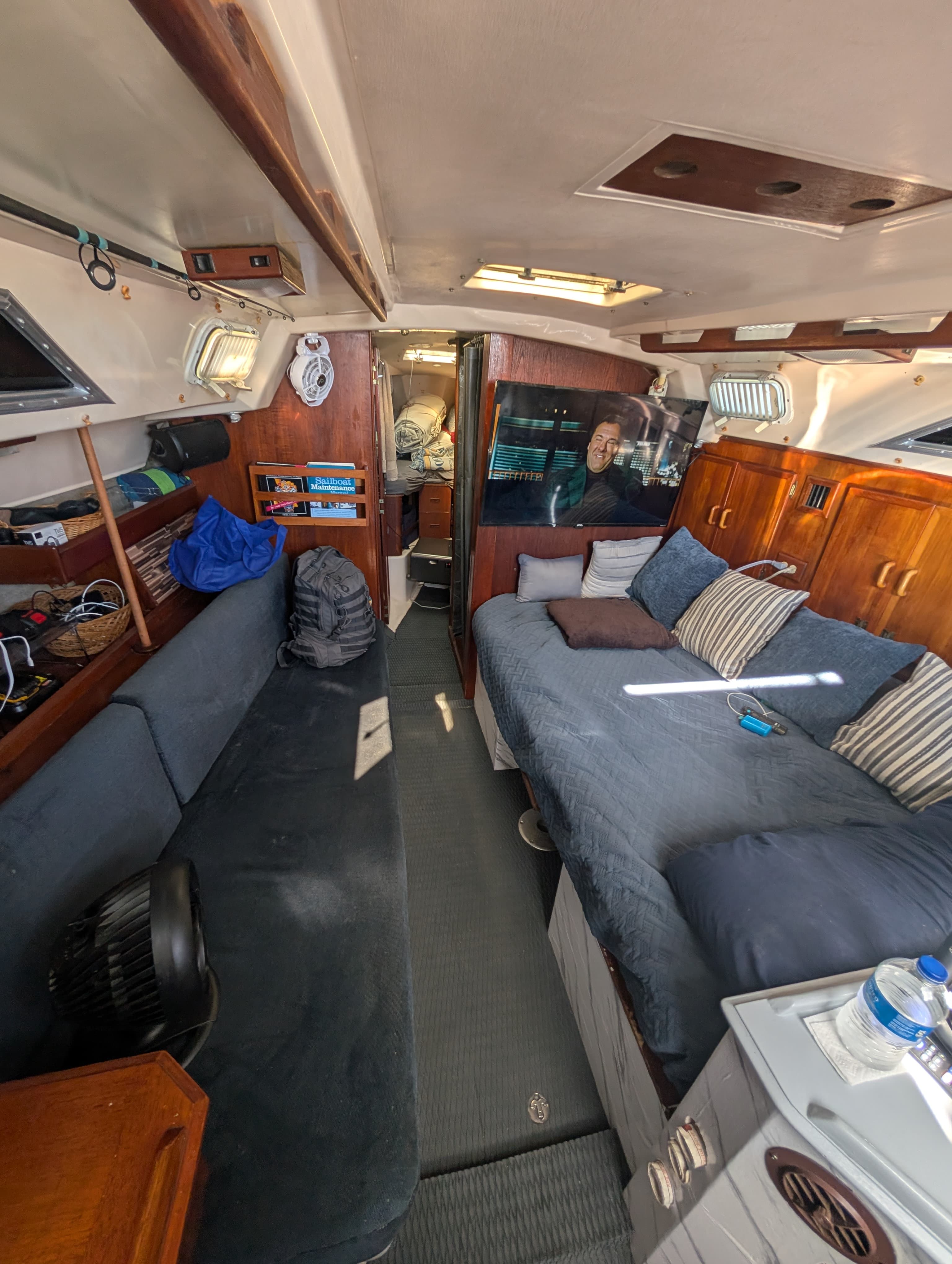 Cozy wood-paneled sailboat cabin interior featuring a blue sofa, bed, and wall-mounted television.