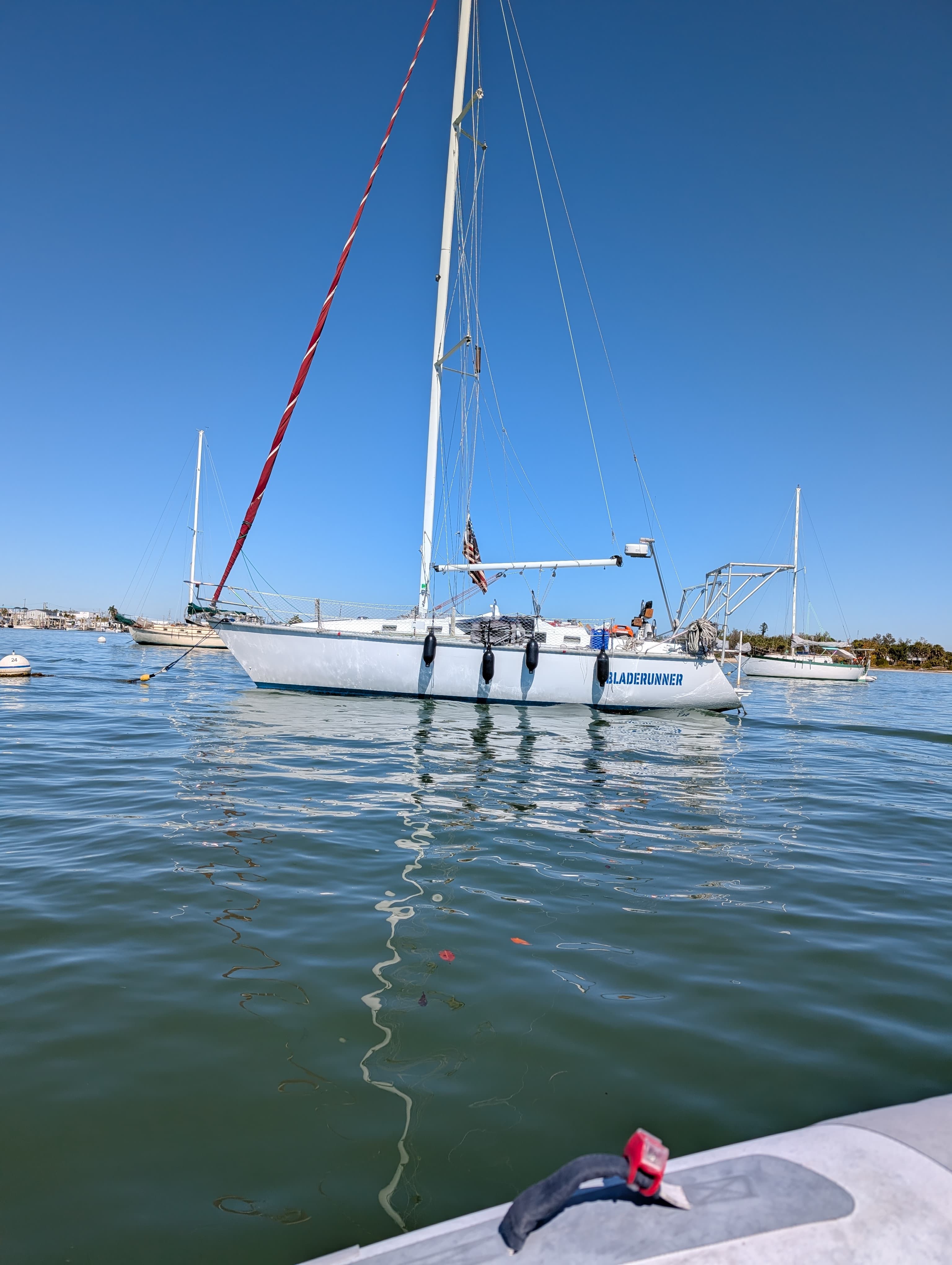 White sailboat named Bladerunner floats on calm blue water under a clear blue sky.