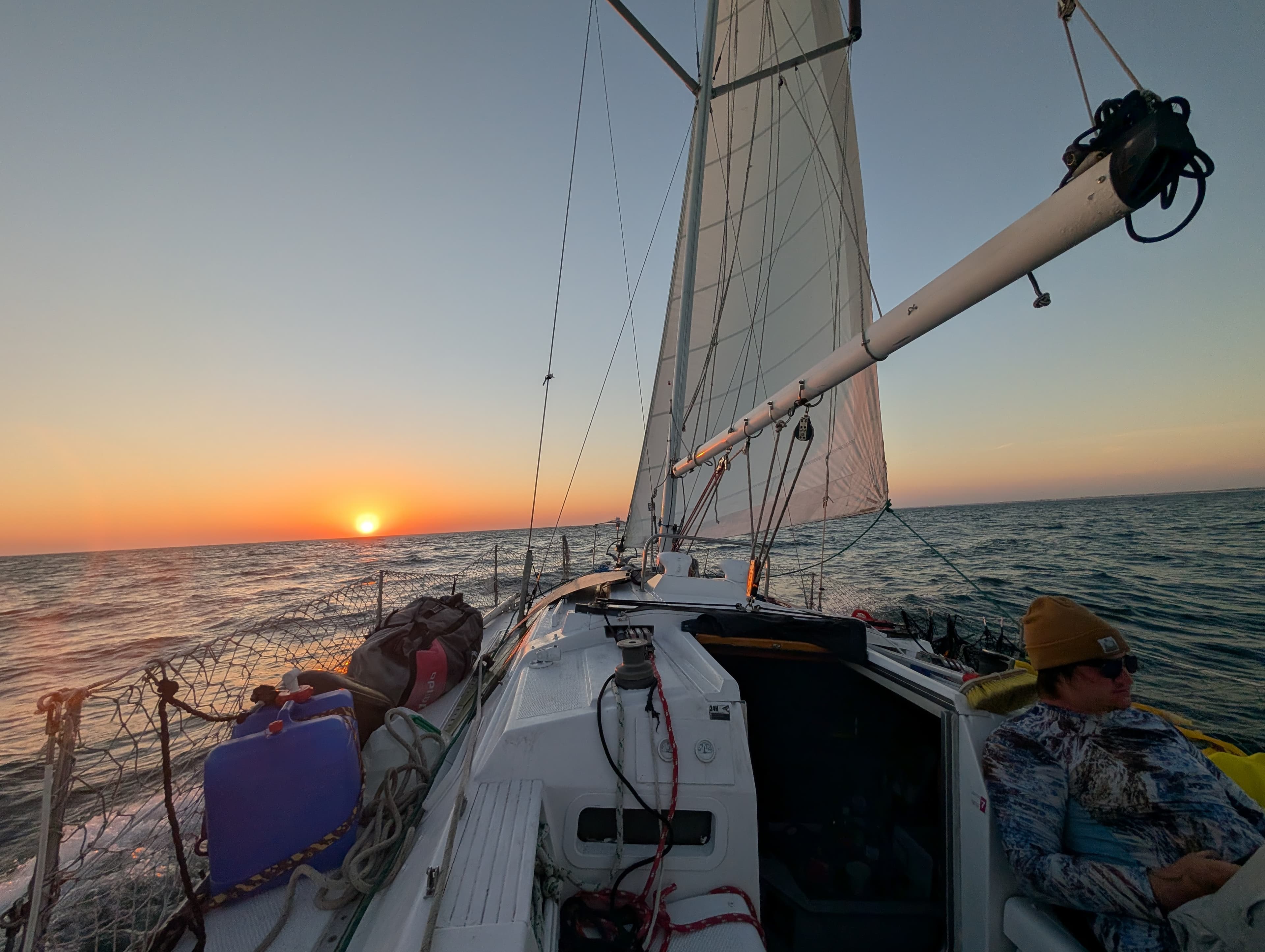 Sailboat cruising on the open sea during a vibrant sunset with a person on deck.