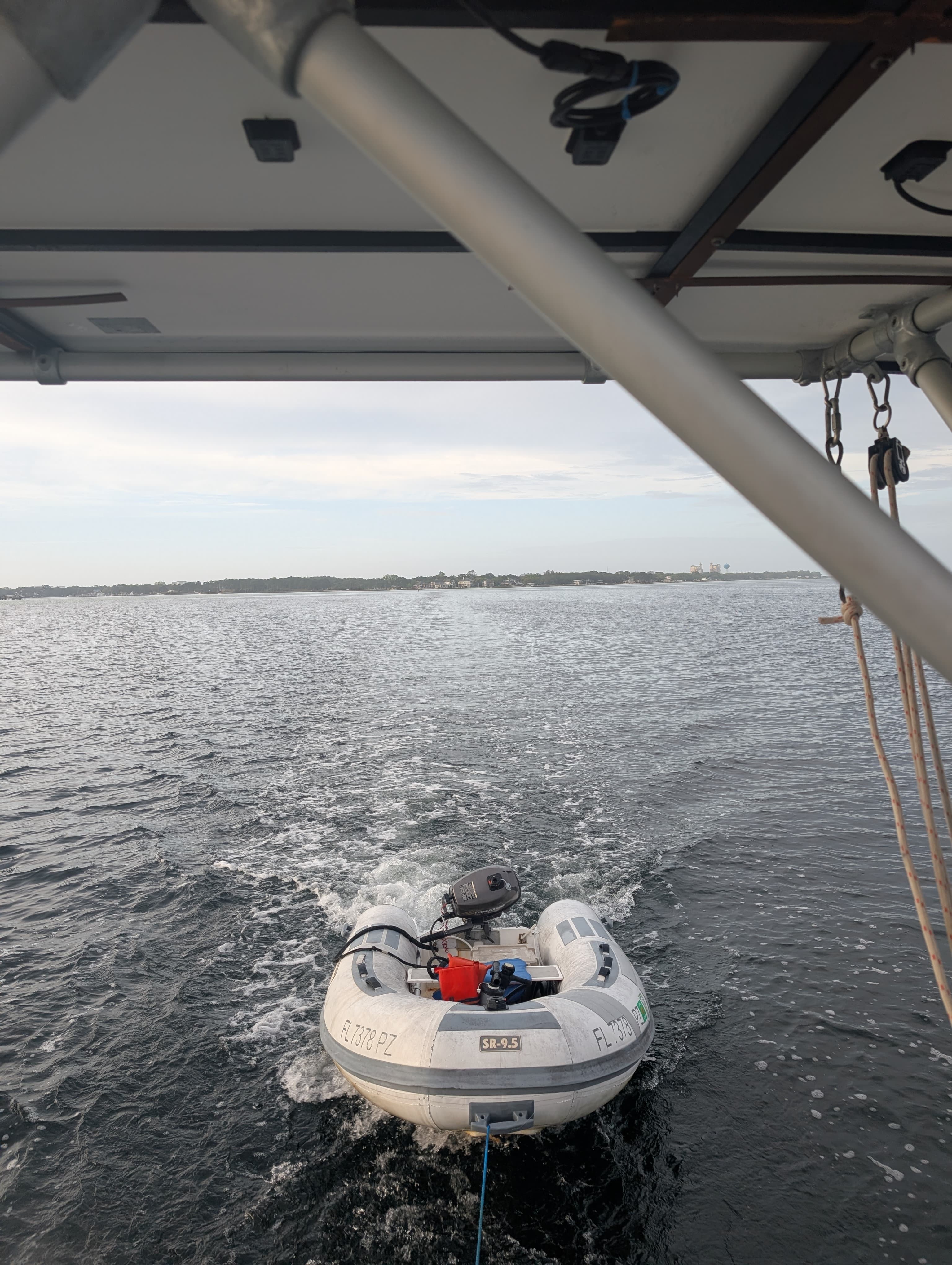 Small inflatable dinghy with an outboard motor towed behind a boat, leaving a white wake.